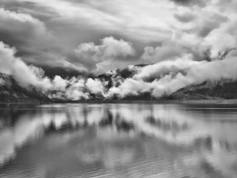 Captivating black and white photo of a lake with dramatic cloud reflections and mountainous backdrop.