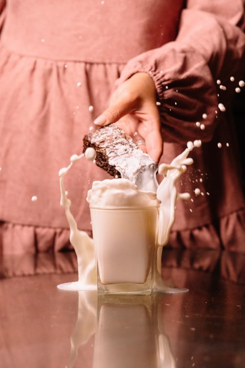 Free A dynamic splash of milk as a chocolate cookie is dropped into a glass on a reflective surface, creating an eye-catching motion. Stock Photo