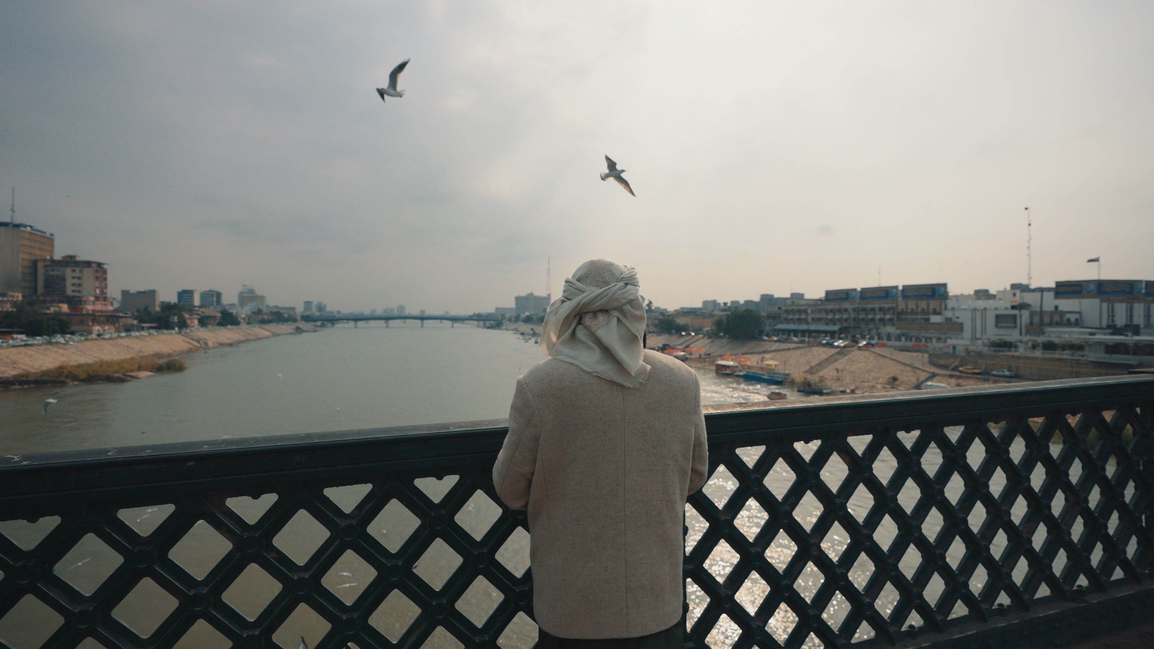 A person in traditional attire looks over the Tigris River from a bridge in Baghdad.