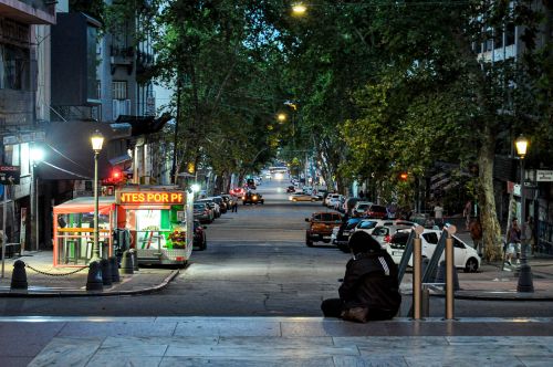 Free Night view of a vibrant street in Montevideo with a food cart and cars lining the road. Stock Photo