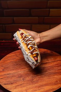 Hand holding a hot dog with savory toppings, perfect for food enthusiasts.