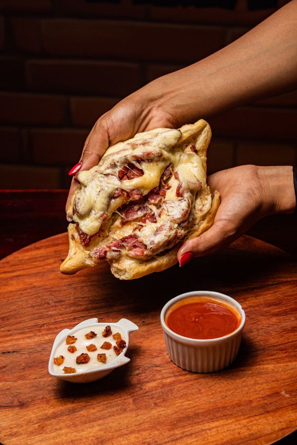 Uma fatia de pizza recheada sendo erguida sobre uma tábua de madeira com molho e temperos à parte.