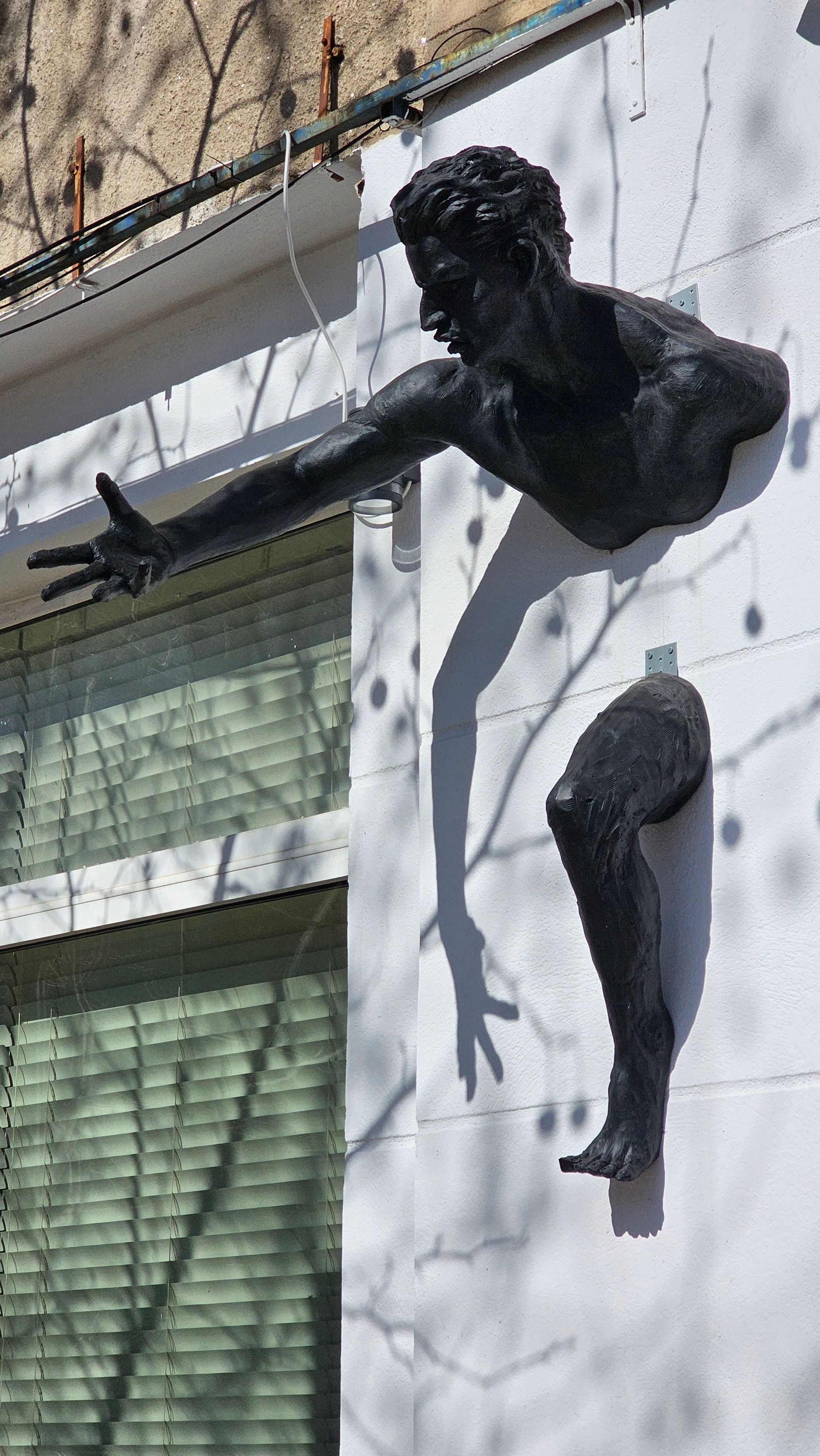 A striking wall sculpture of a human figure displayed outdoors in Bucharest, Romania.