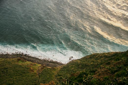 Sunset aerial view of Madeira's coastline with waves crashing on rocky beaches and lush cliffs.