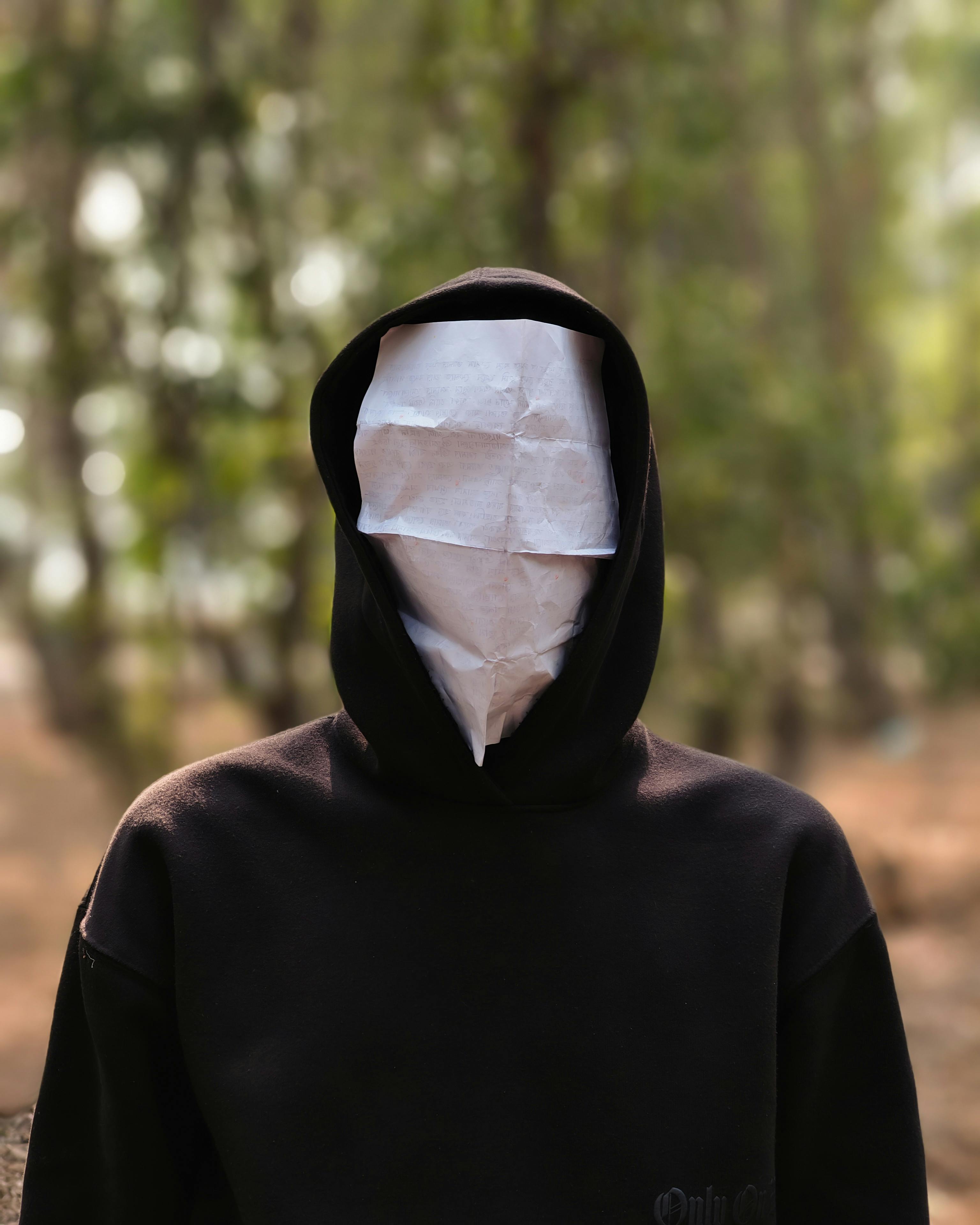 Gratuit Figură cu glugă și fața acoperită de hârtie într-un decor forestier, evocând mister. Fotografie de stoc