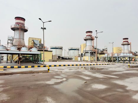 A modern industrial power plant with chimneys and wet pavement, photographed after rain.