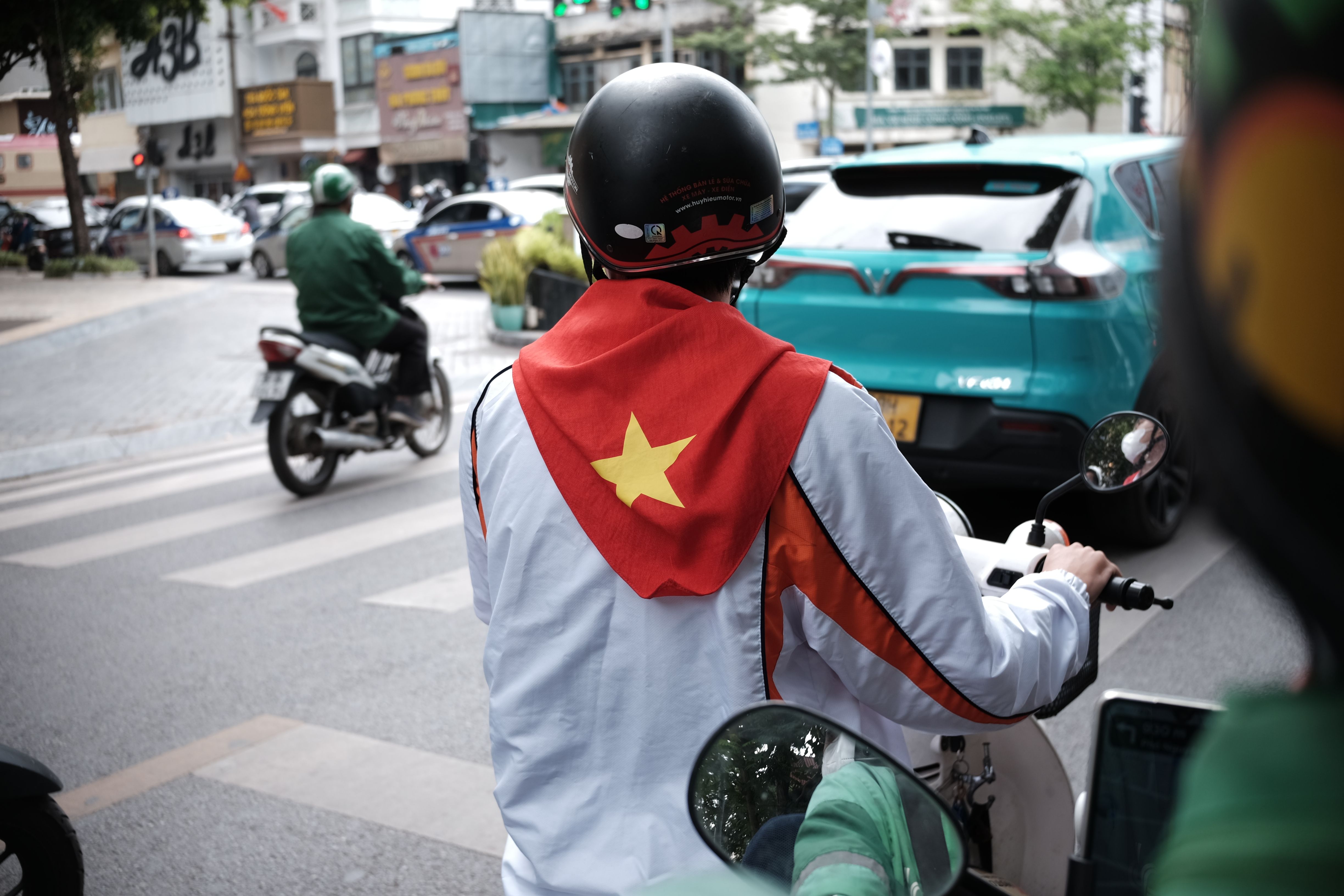 Motorbike rider with Vietnam flag at a city intersection, showcasing urban traffic.