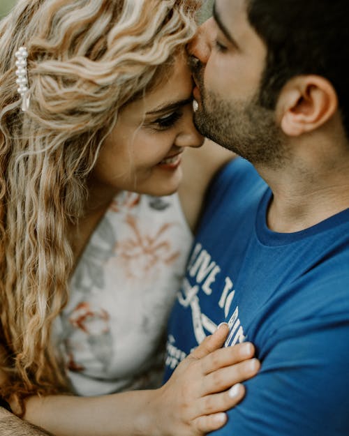 Man in Blue Crew Neck Shirt Kissing Woman in White and Blue Floral Dress