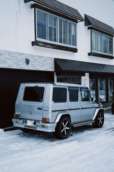 Silver luxury SUV parked in a snowy street in Sapporo city, capturing the winter urban setting.