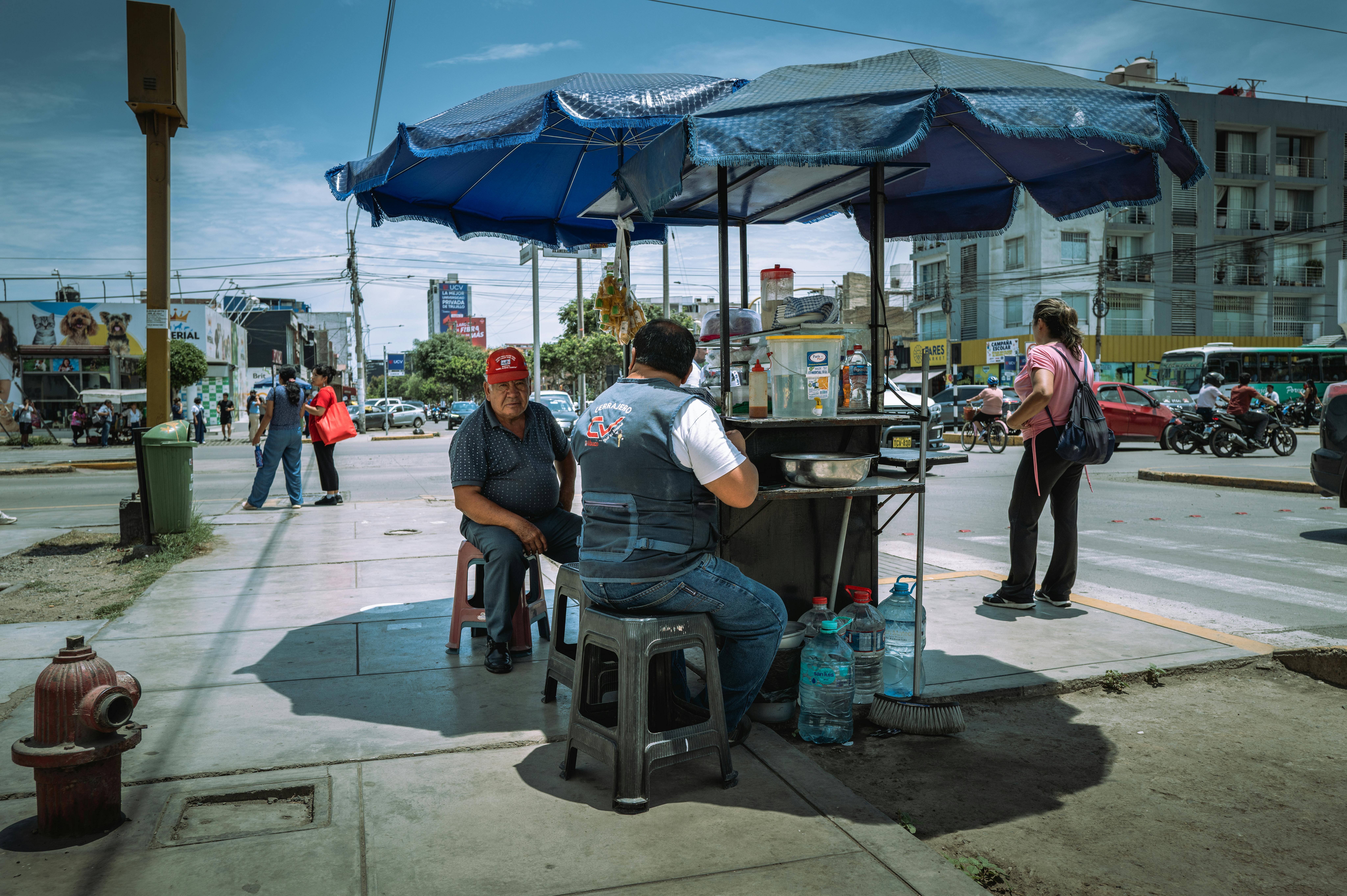 A bustling street food stand in Trujillo, Peru under a blue canopy on a sunny day.