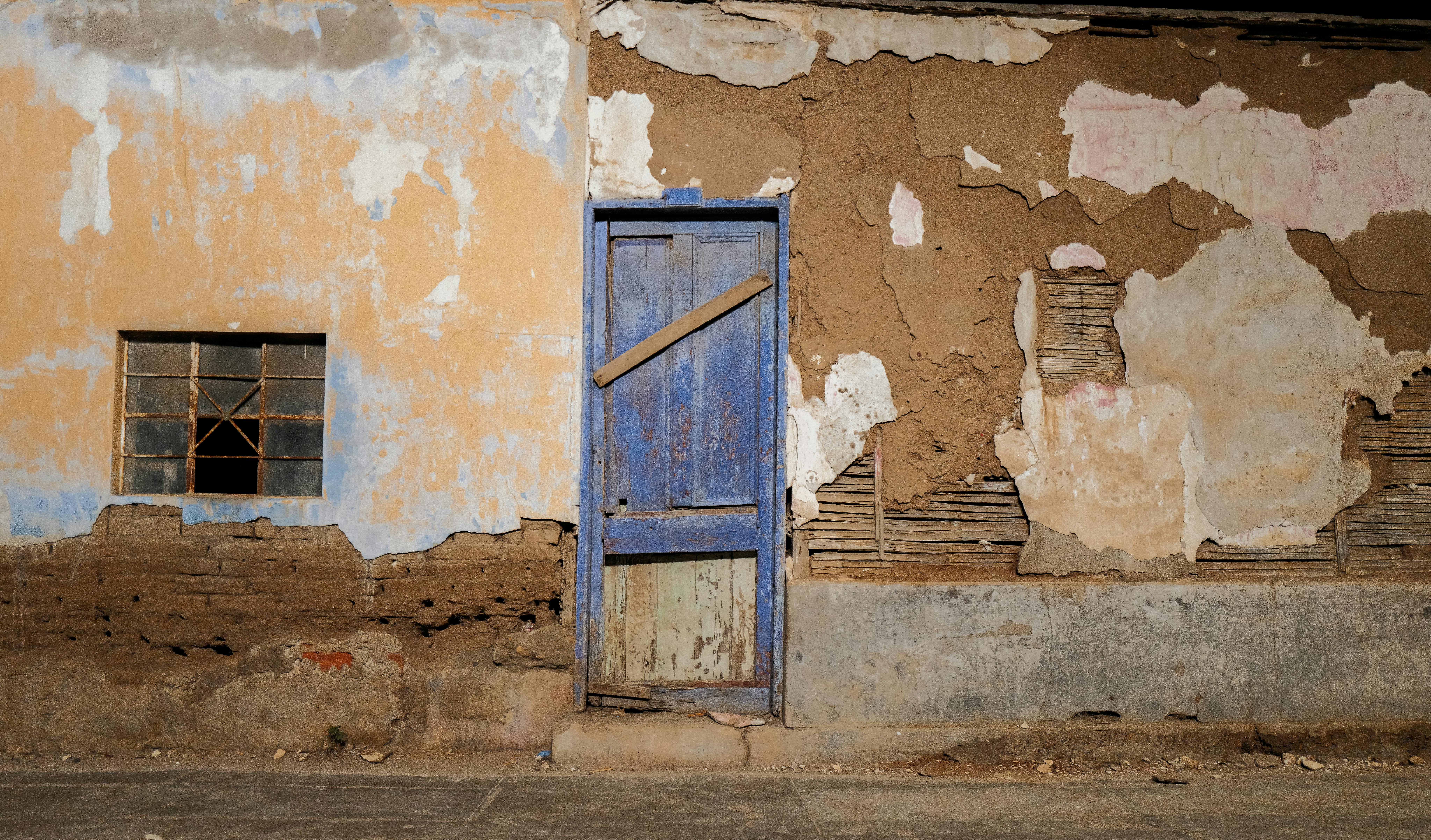 A weathered blue door on a rustic, adobe wall in Trujillo, Peru under the daylight.