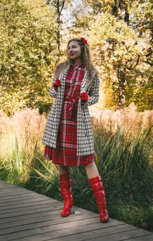Stylish woman in red plaid dress and boots enjoying a sunny autumn day in the park.