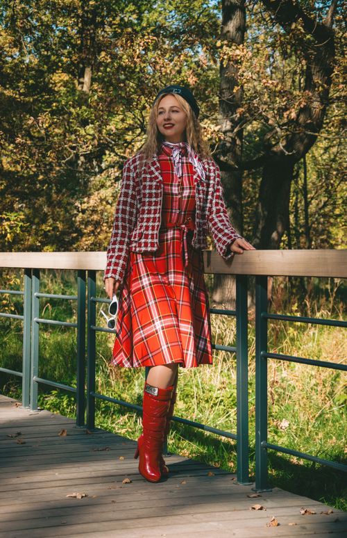 Free Stylish woman in plaid coat and red boots standing on a bridge in a lush autumn park. Stock Photo