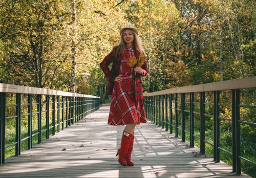 Free Woman in a red plaid dress holding autumn leaves on a park bridge during fall. Stock Photo