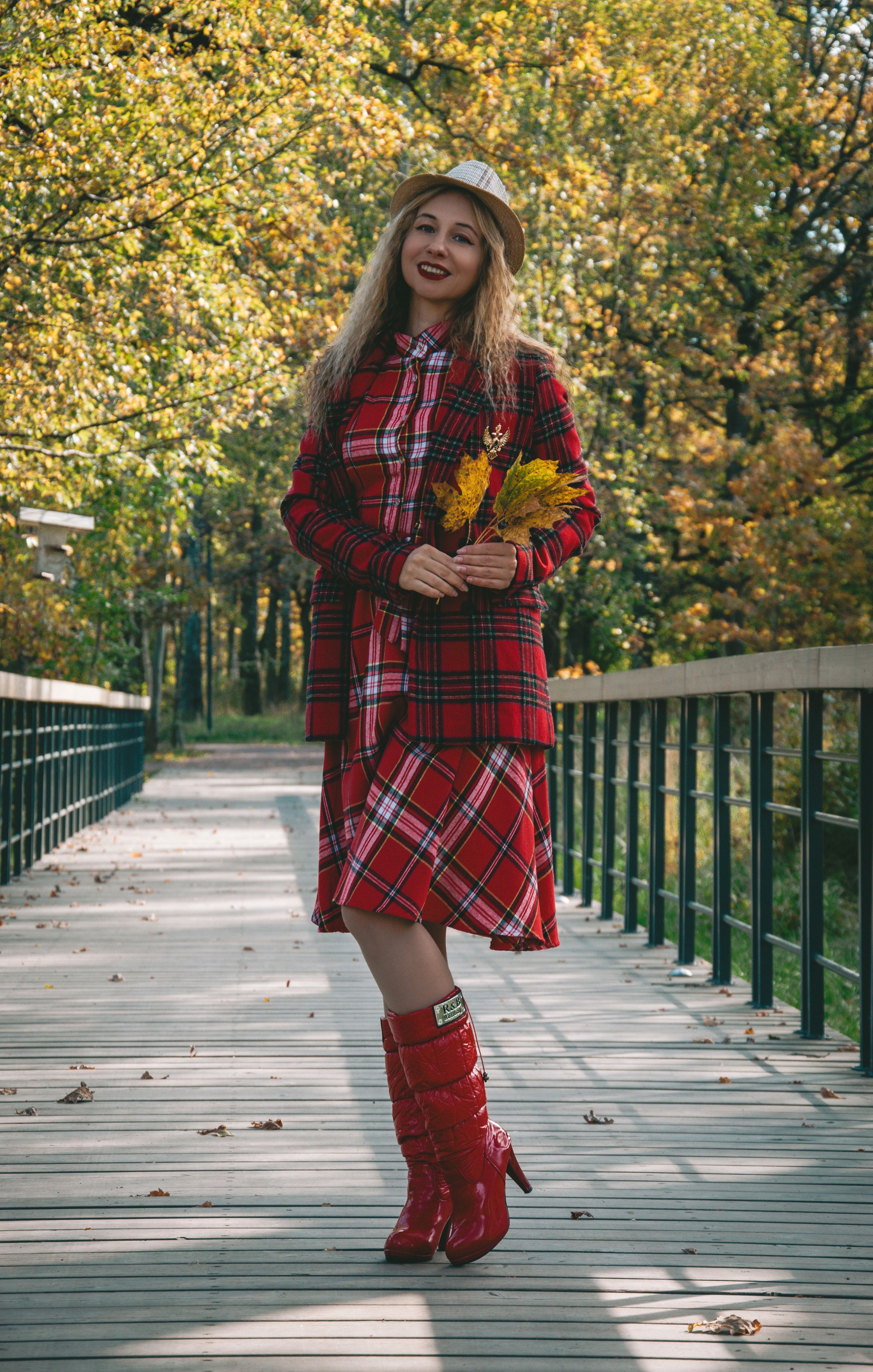 Stylish woman in plaid outfit walking on a sunny fall day, holding autumn leaves.