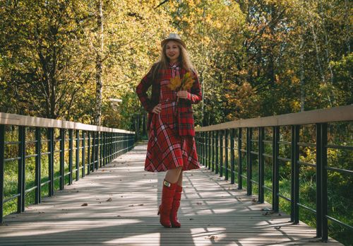 Free Smiling woman in red tartan dress and boots holding autumn leaves on a bridge Stock Photo