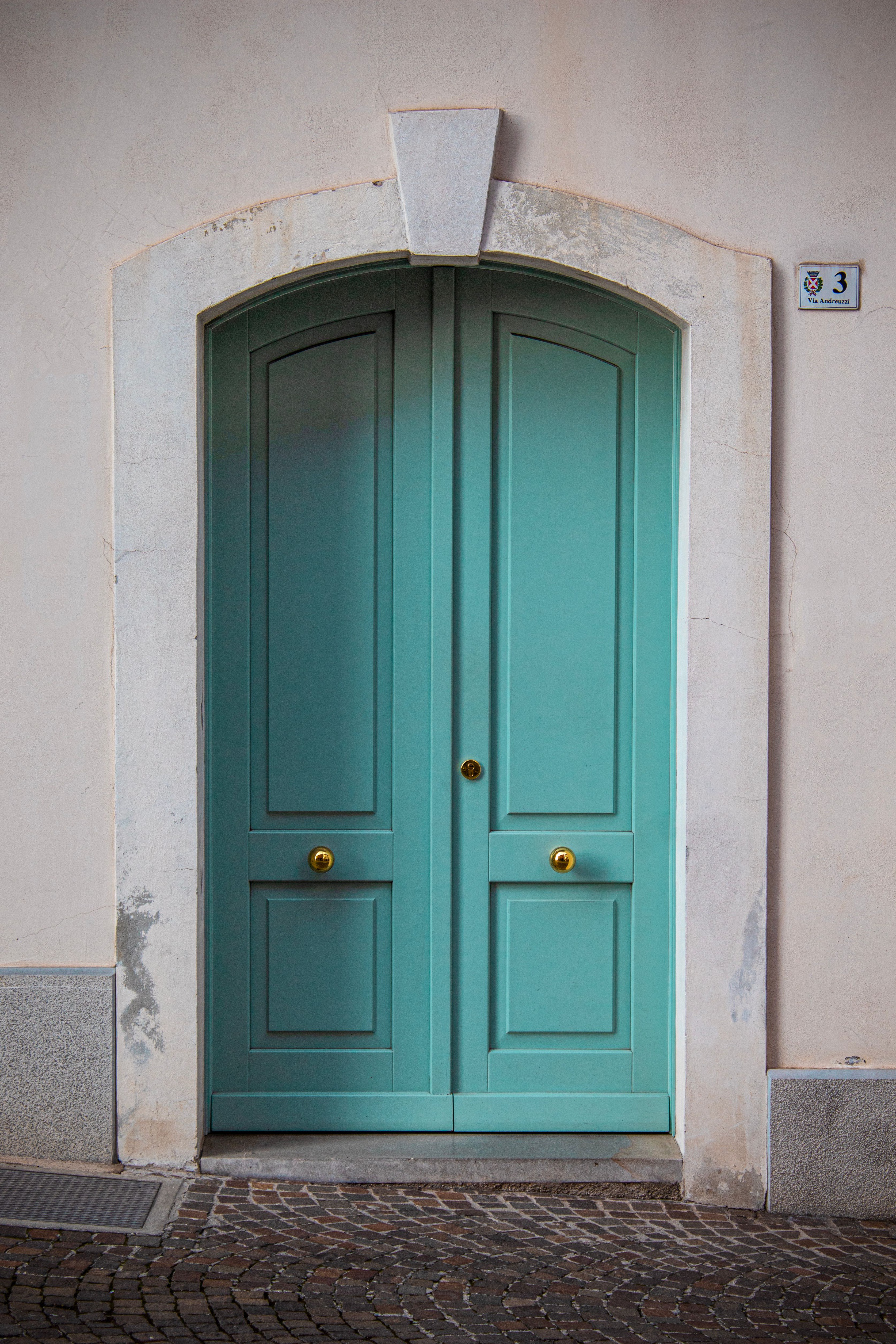 A beautiful teal door with arched frame in San Daniele del Friuli, Italy.