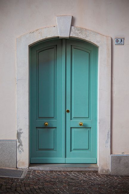 A beautiful teal door with arched frame in San Daniele del Friuli, Italy.
