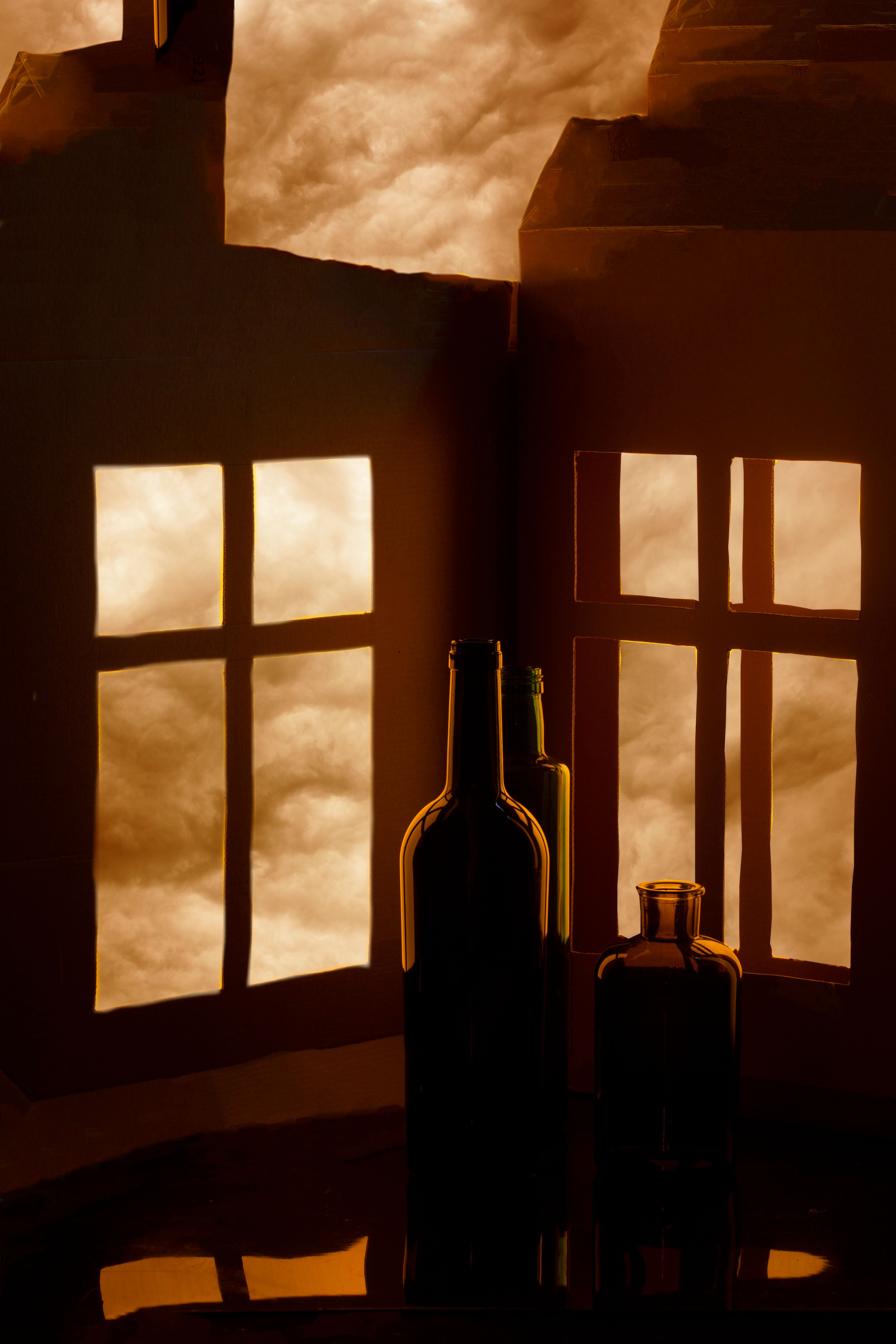 Silhouetted bottles against a warm, abstract backdrop with window shadows, creating a dramatic atmosphere.