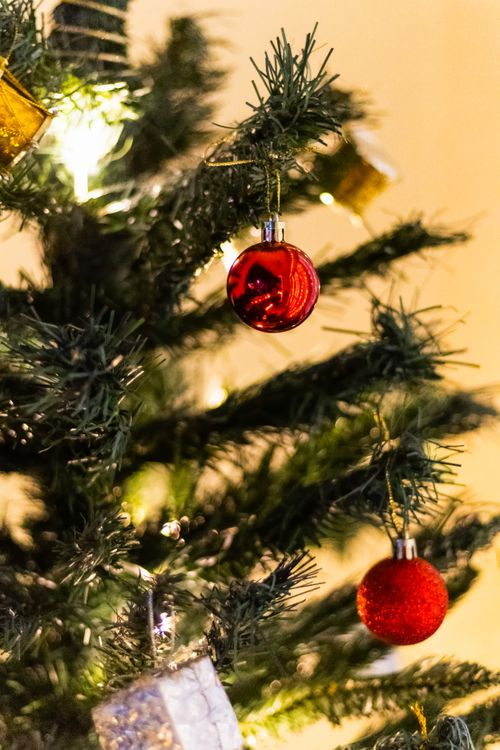 Free Close-up of a decorated Christmas tree with red ornaments and golden lights, creating a festive atmosphere. Stock Photo
