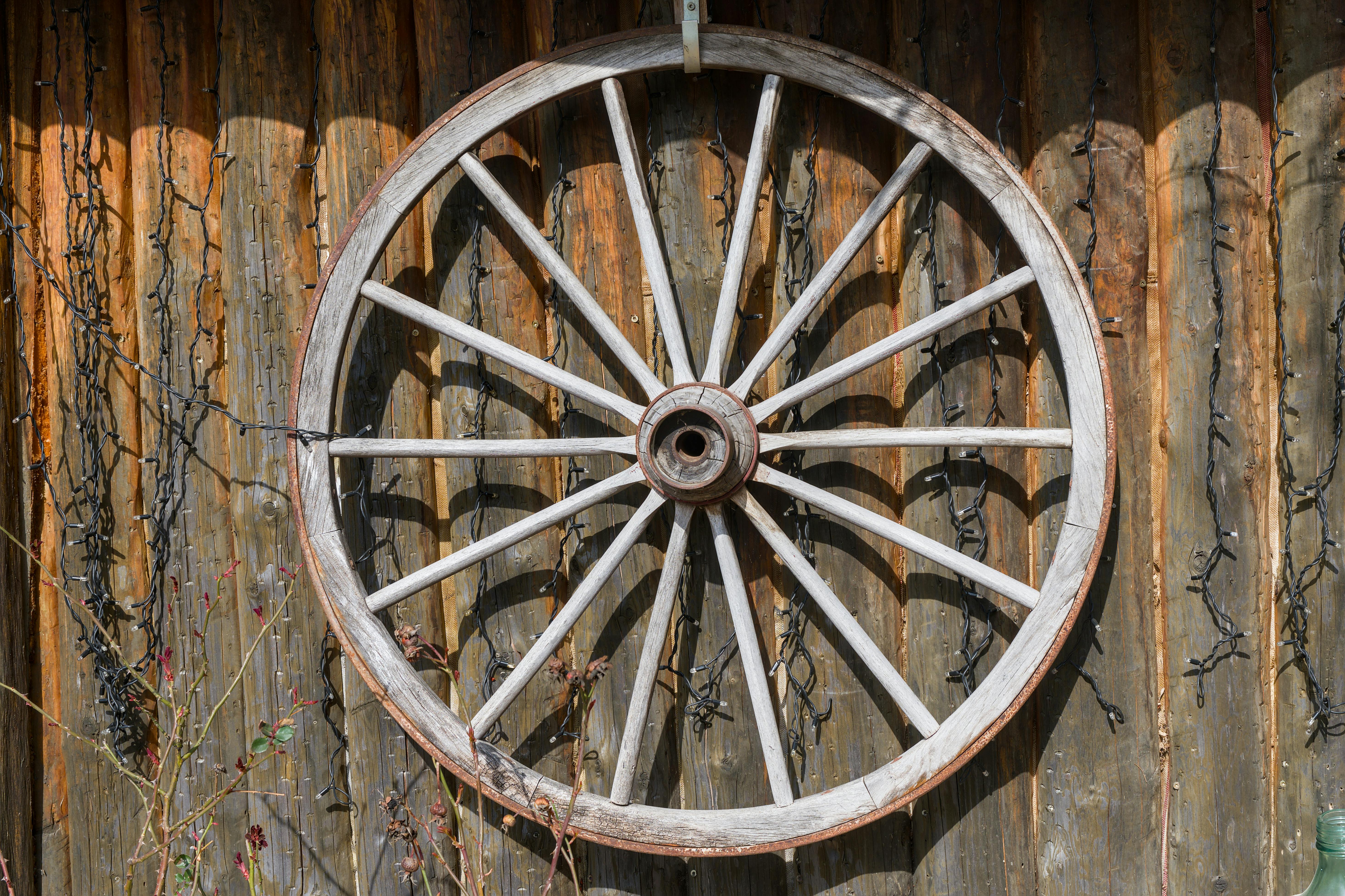Ücretsiz Eski bir ahşap araba tekerleği, rustik bir ahır duvarına monte edilerek nostaljik bir estetik yaratıyor. Stok Fotoğraflar