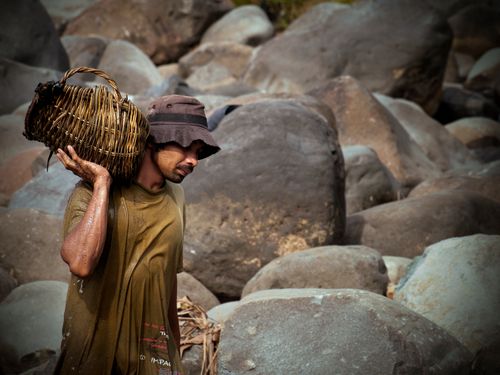 Free A man in West Sumatra, Indonesia, carries a woven basket across a rocky landscape. Outdoors scene. Stock Photo