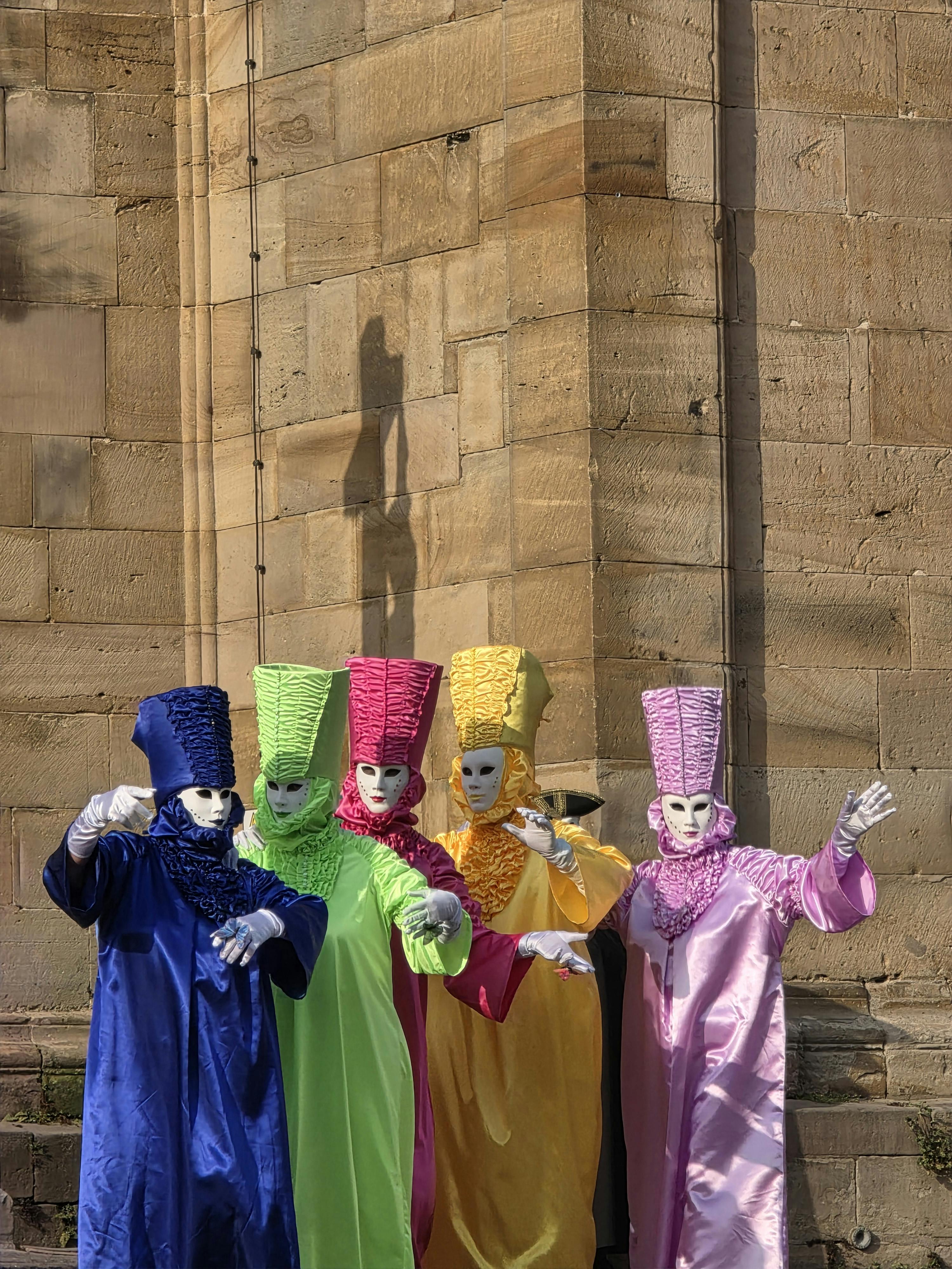 Gratis Costumi di carnevale sgargianti con maschere sullo sfondo di un antico muro di pietra, a raffigurare una vivace parata. Foto a disposizione