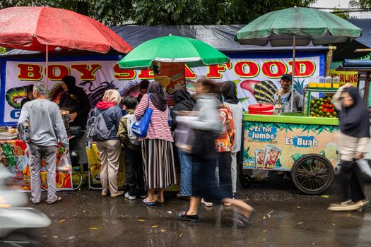 Vibrant street food market with people in motion, colorful umbrellas, and a food cart.