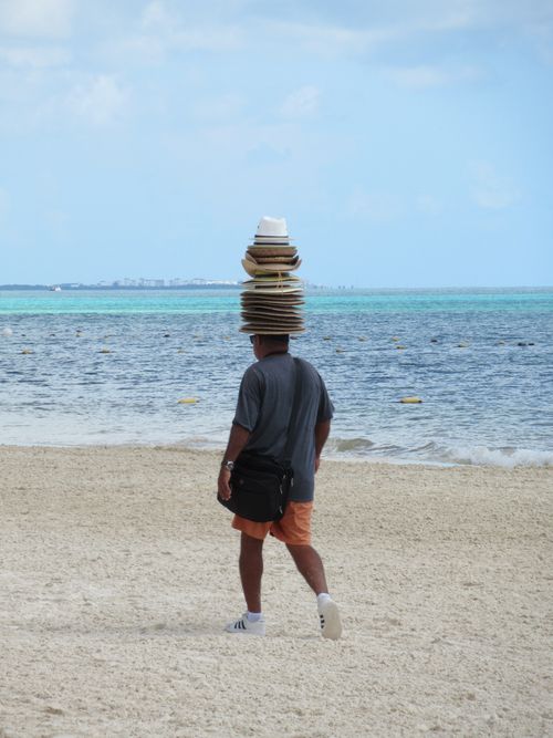 Free A street vendor balancing multiple hats on the beach in Mexico, showcasing impressive skill. Stock Photo