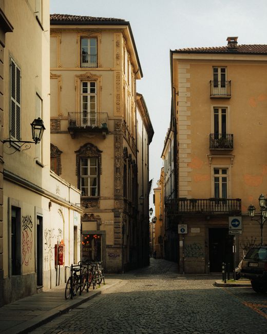 Explore a picturesque narrow street in Turin, Italy, showcasing classic architecture under the warm daylight.