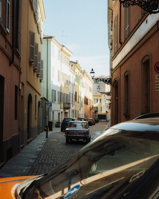 Charming view of a vintage car on a sunlit street in Parma, Italy.