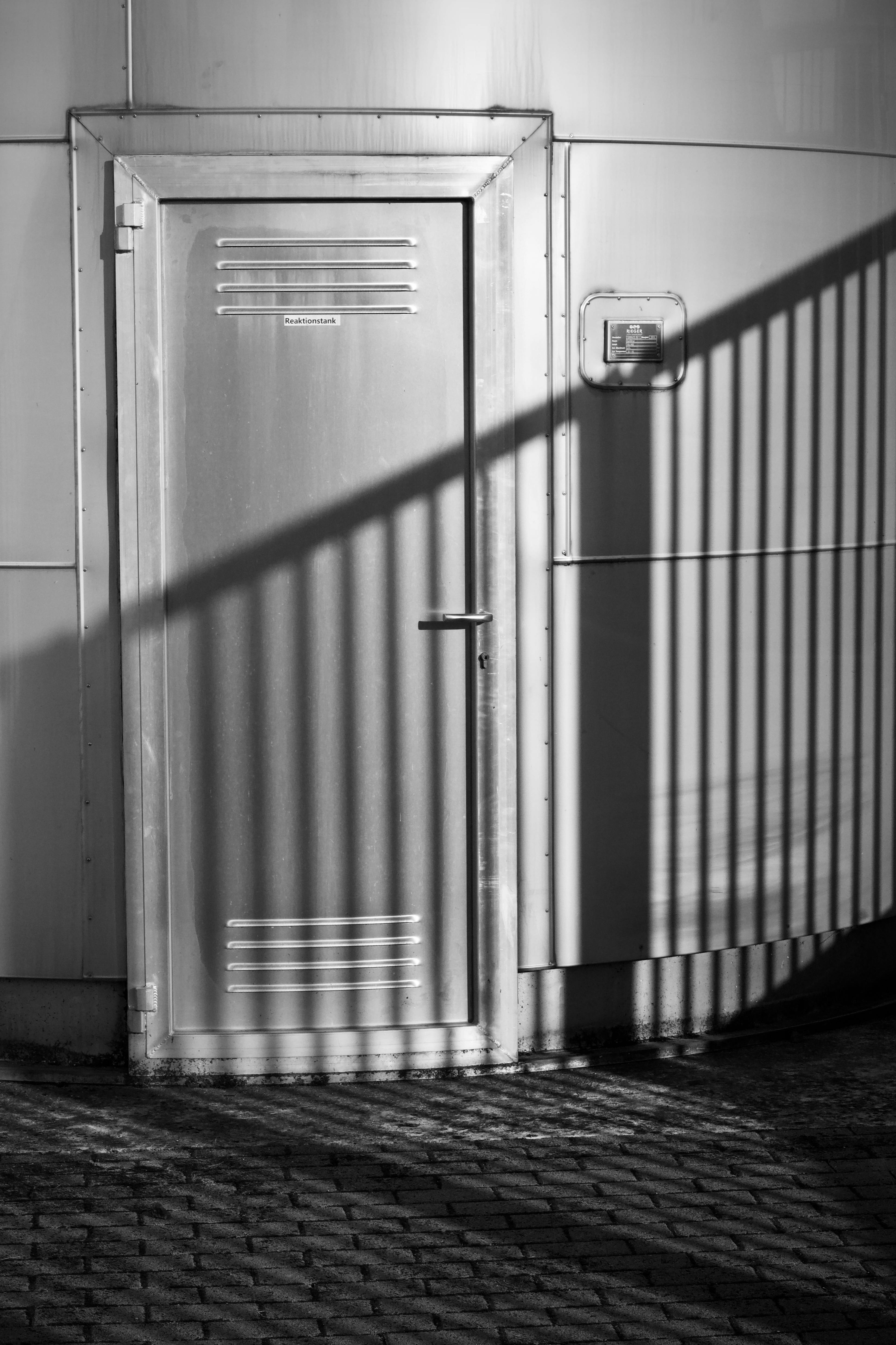 Zadarmo Čiernobiely obrázok priemyselných kovových dverí s výraznými tieňovými vzormi, ktorý vytvára moderný a minimalistický vzhľad. Fotka z fotobanky