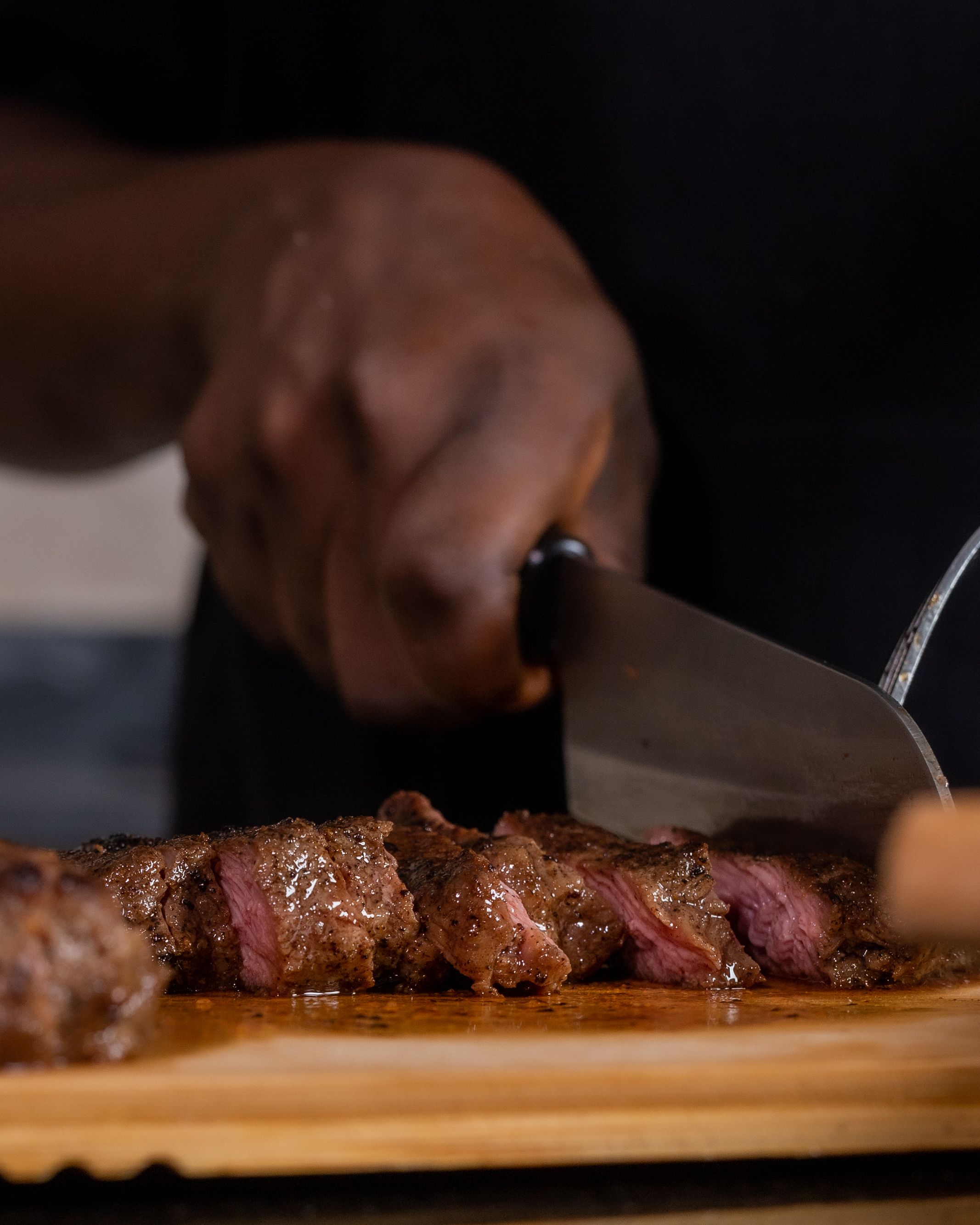Couteau qui tranche une pièce de bœuf grillée sur une planche, tranches saignantes, fond sombre
