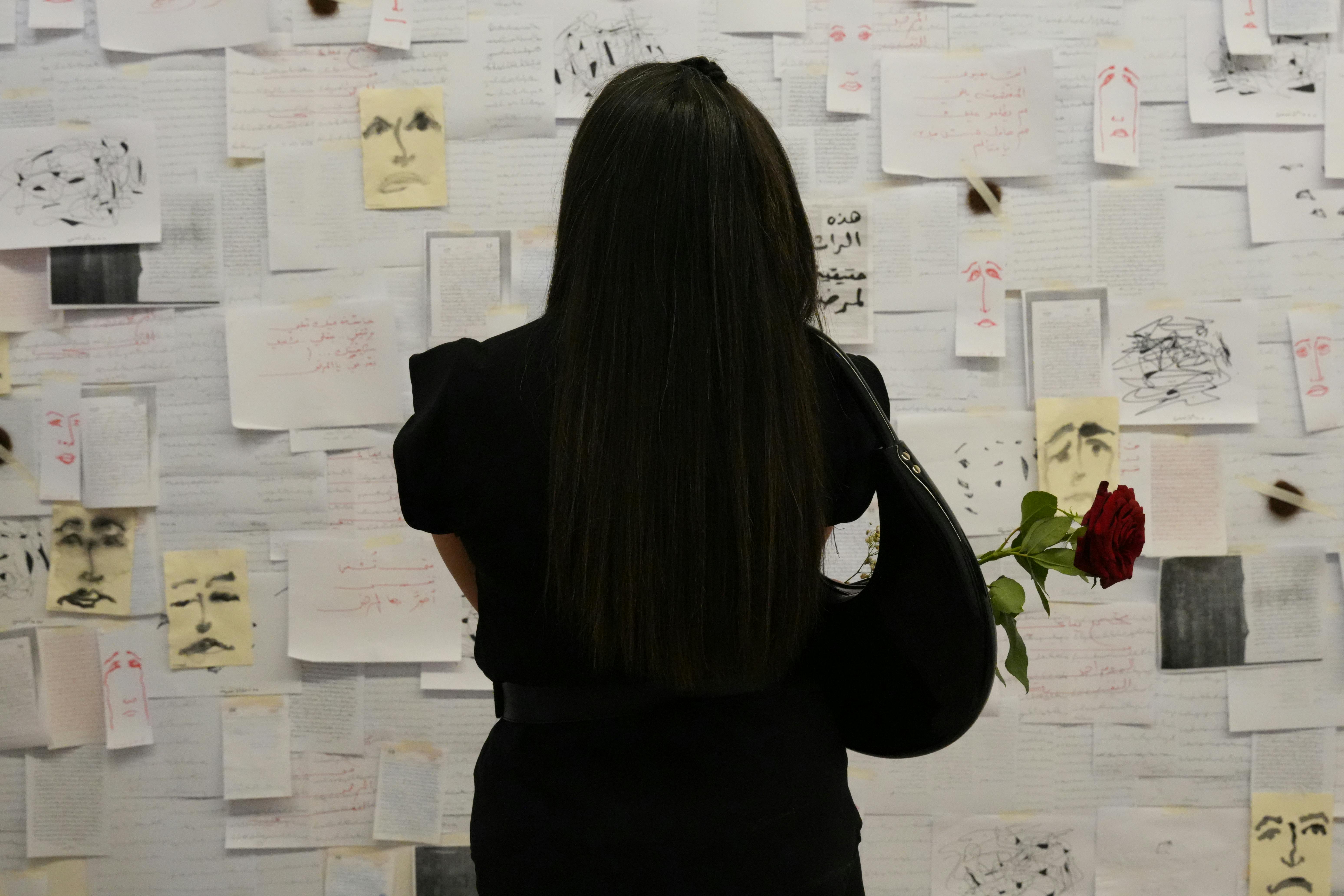 Gratis In una galleria di Damasco, una donna con una rosa in mano osserva una parete artistica ricoperta di appunti e disegni. Foto a disposizione