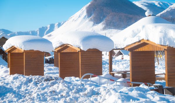 Wooden cabins blanketed with snow in a serene mountain landscape, capturing the essence of winter wonderland.