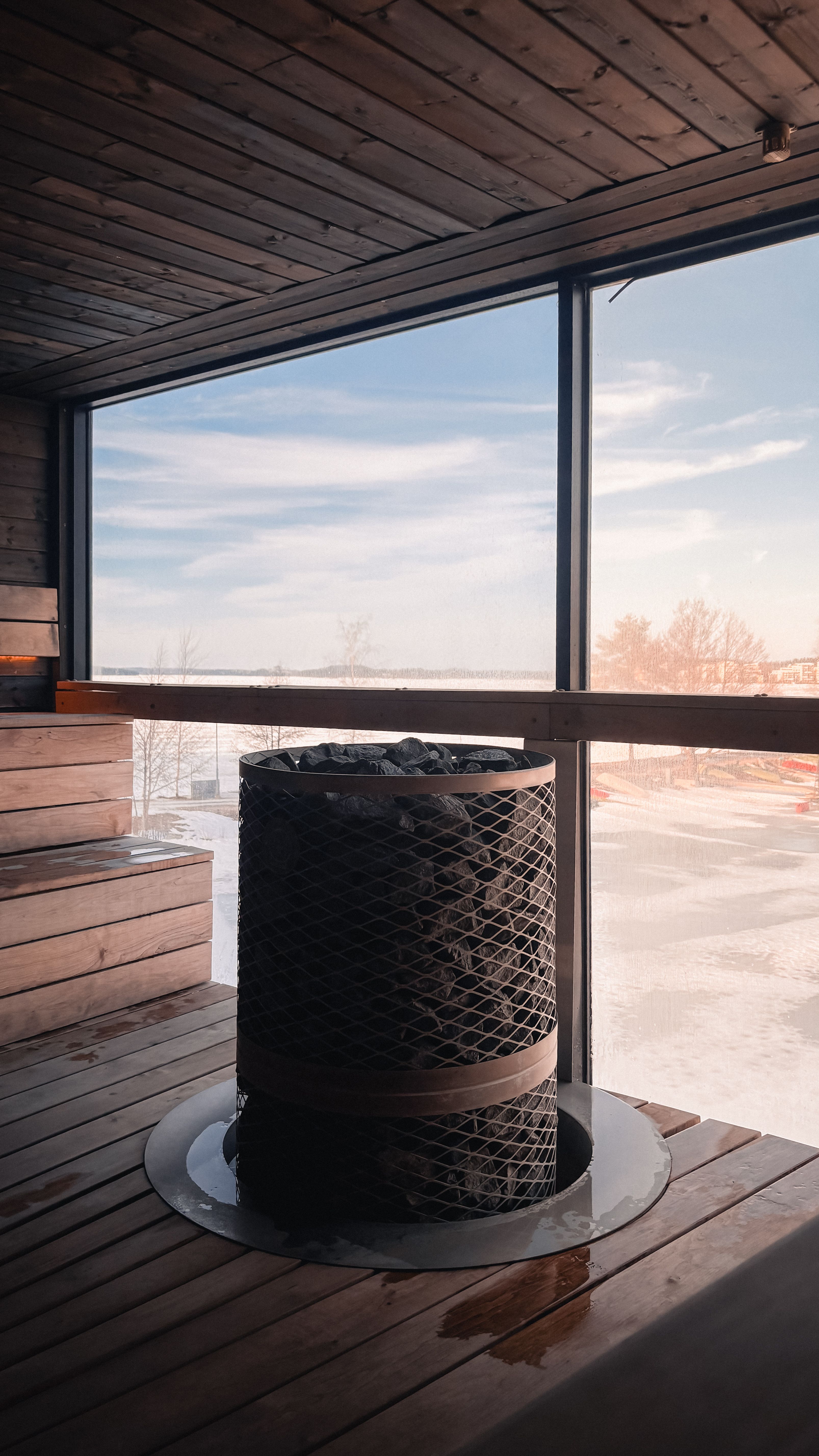 A wooden sauna interior with a wide window looking out over a snowy winter landscape.