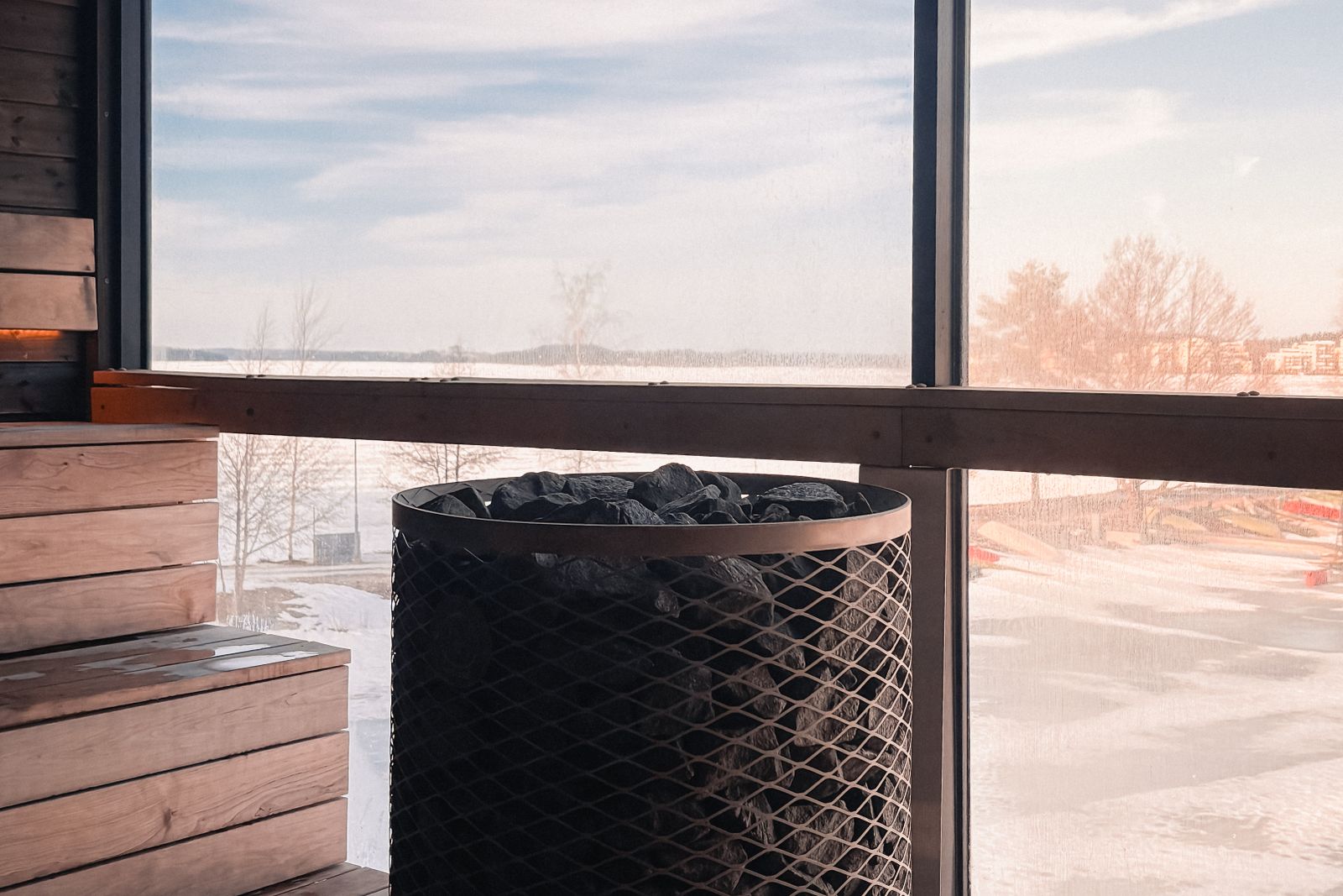 A wooden sauna interior with a wide window looking out over a snowy winter landscape.