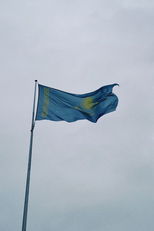 Free The national flag of Kazakhstan fluttering on a pole against a clear sky, symbolizing pride and unity. Stock Photo