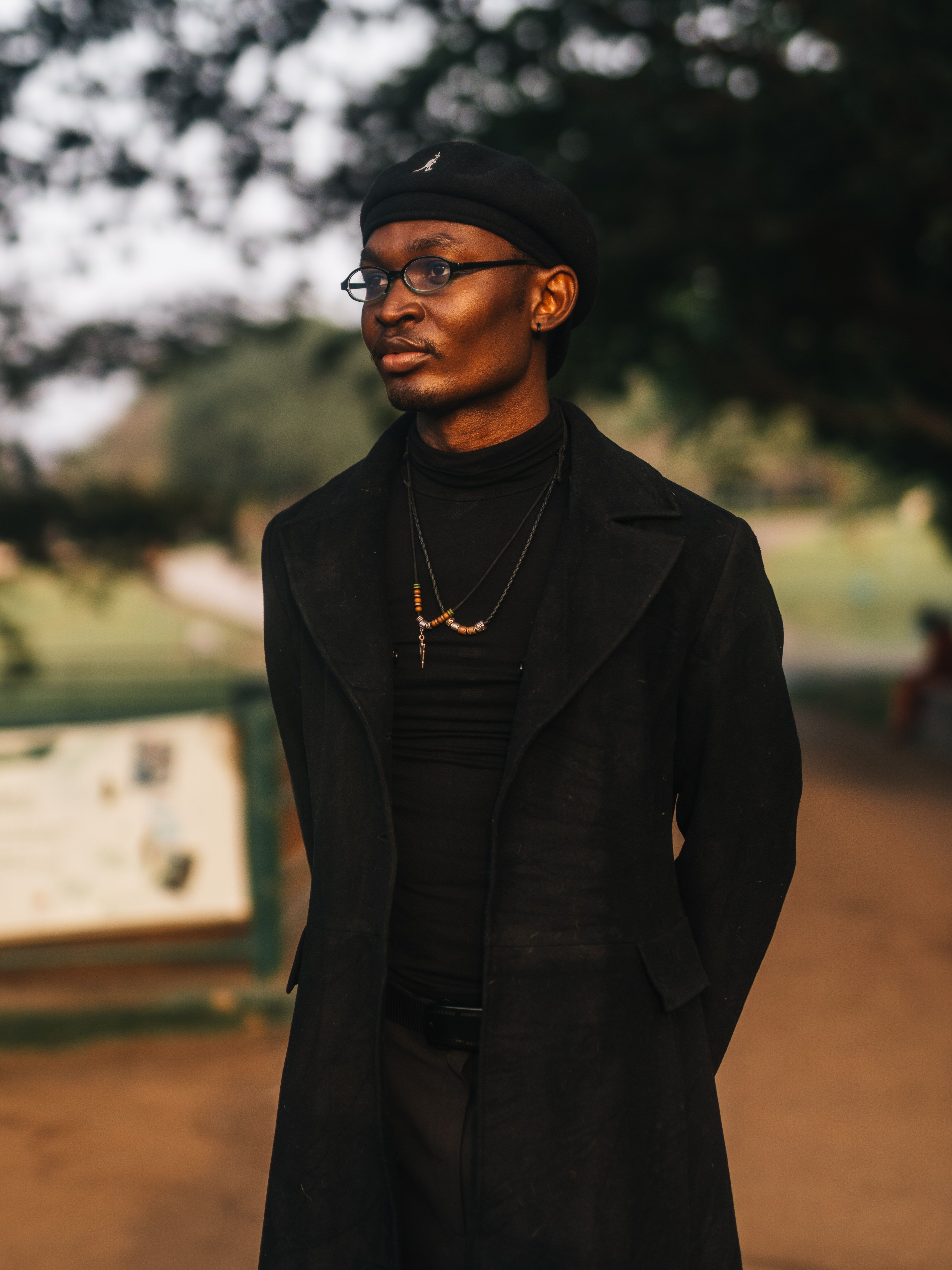 A fashionable man in a black outfit poses confidently in a park in Abuja, Nigeria.