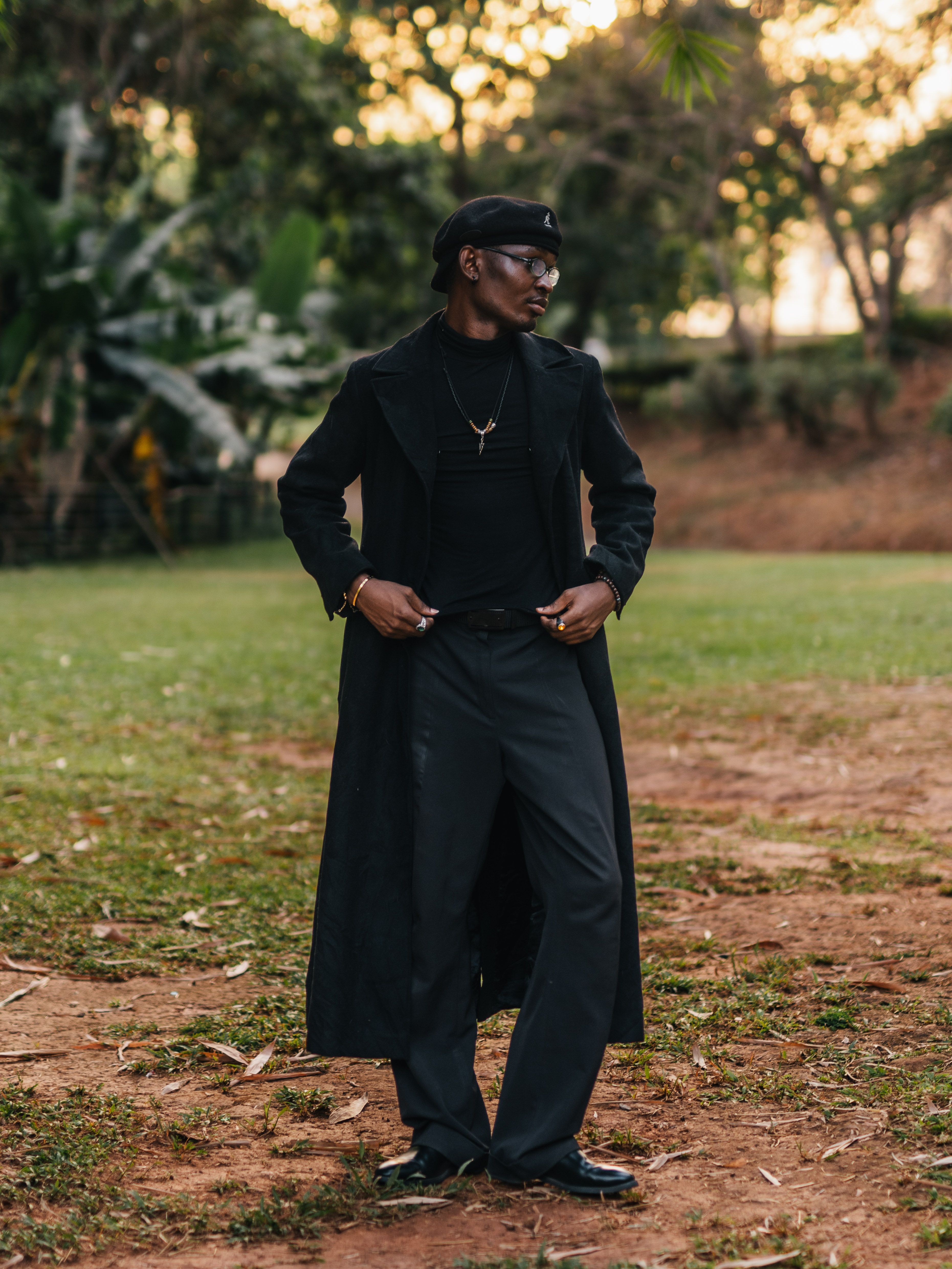 Elegant man in black ensemble posing in a serene park in Abuja, Nigeria.