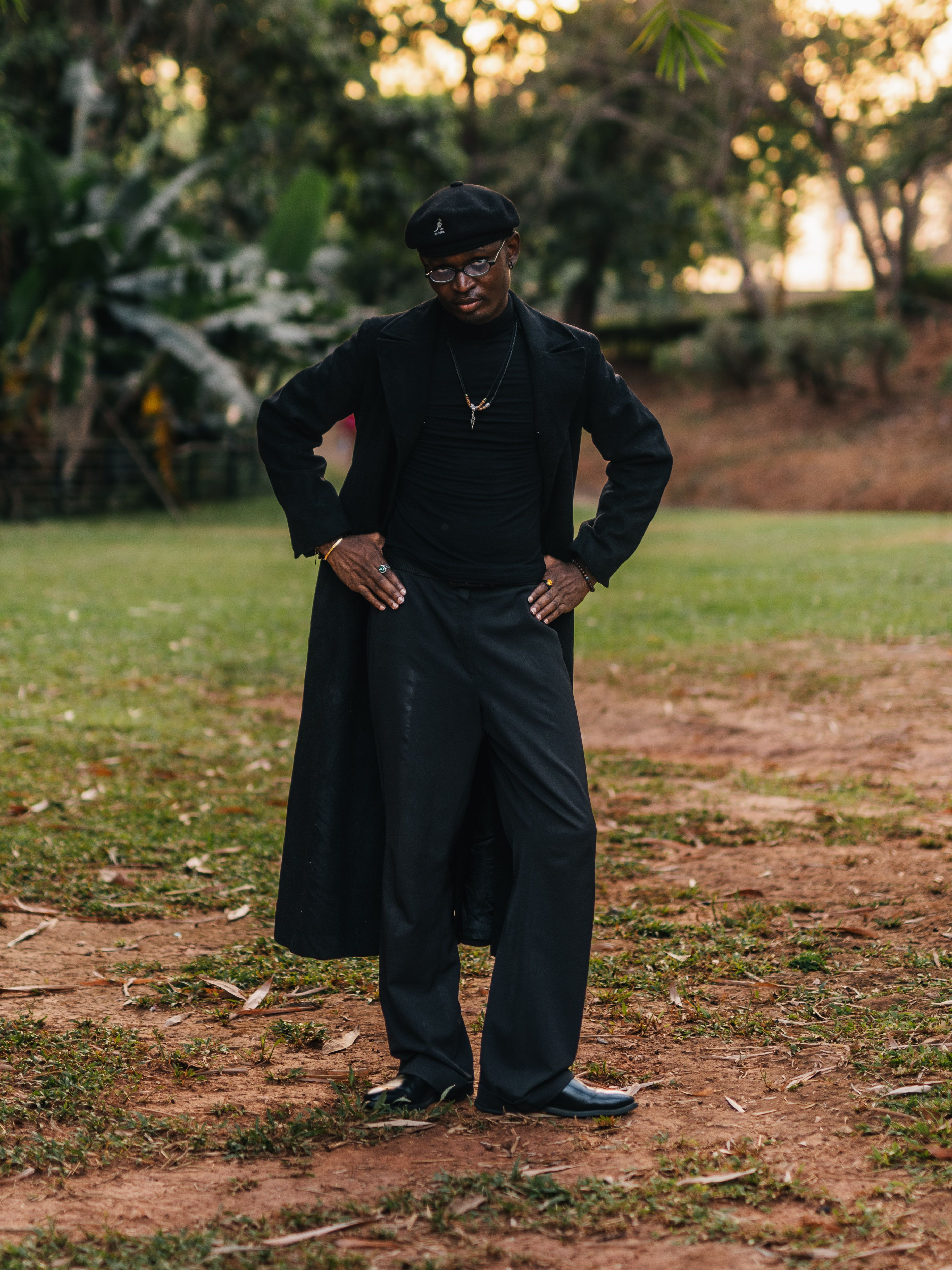 Elegant man in black attire posing confidently in a lush outdoor setting in Abuja.