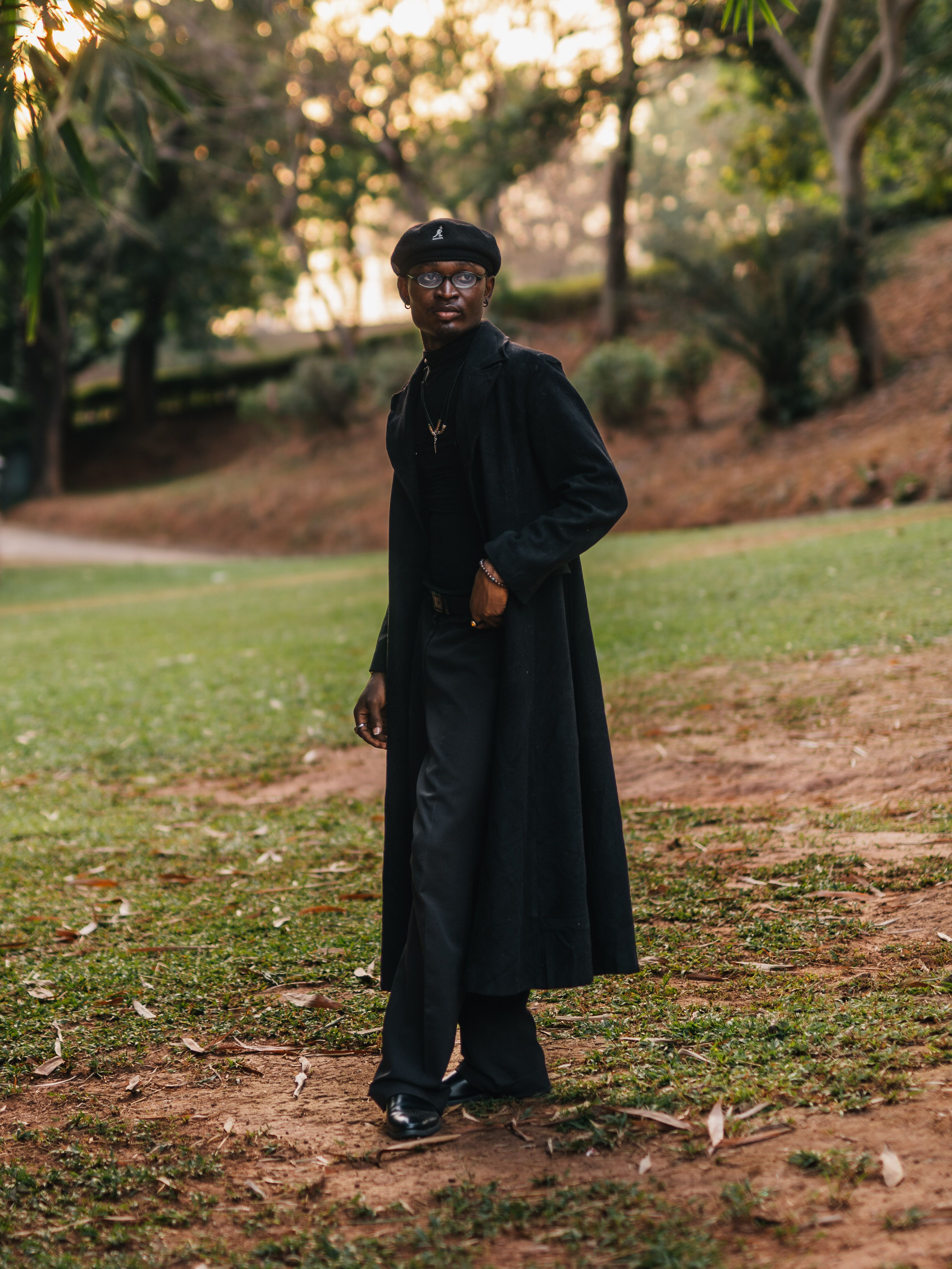Person wearing black coat and hat walking in a lush park in Abuja, Nigeria.