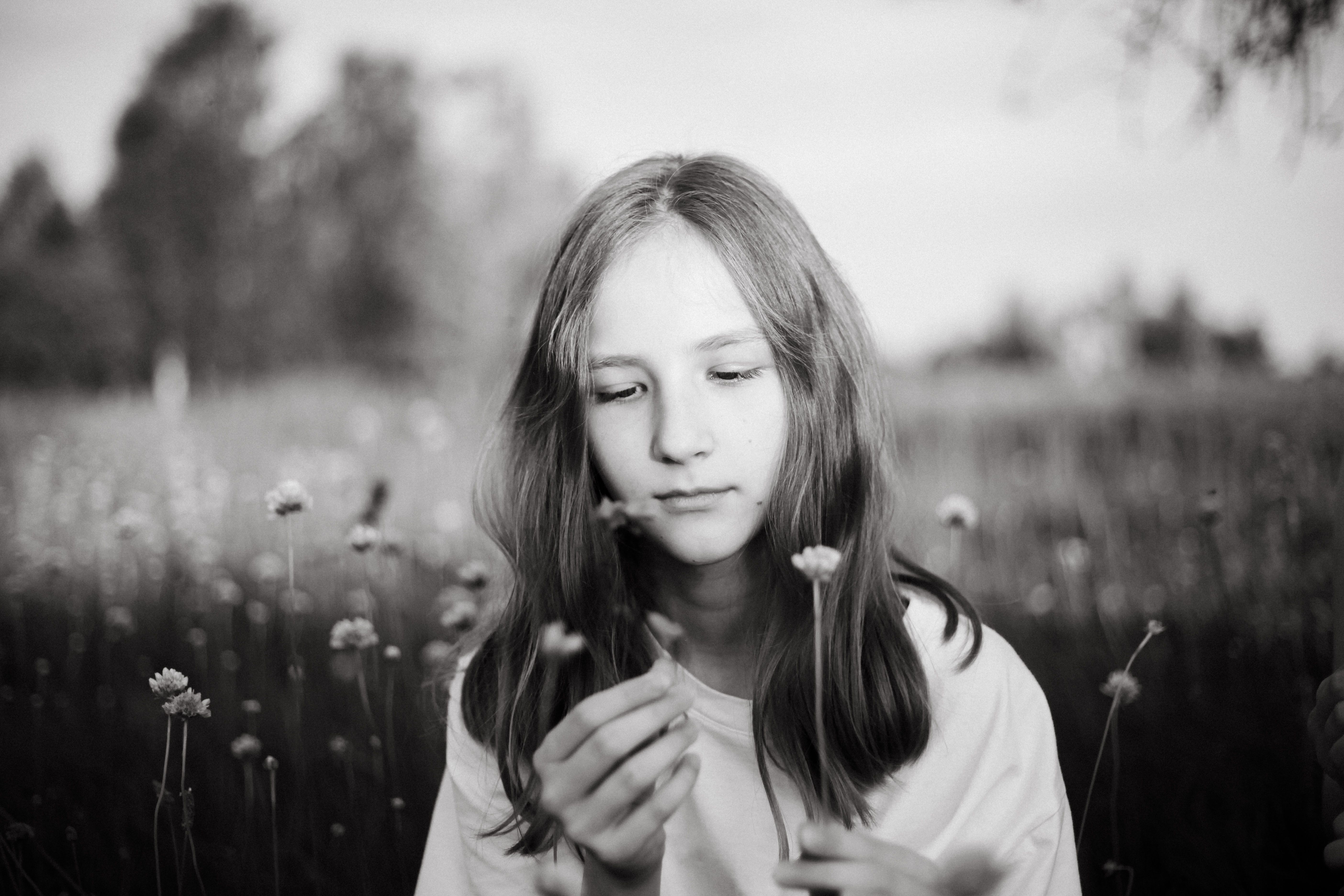 Black and white portrait of a girl holding a flower in a meadow, evoking tranquility.
