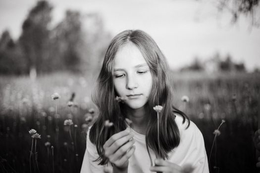 Black and white portrait of a girl holding a flower in a meadow, evoking tranquility.