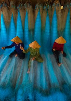 Three workers create fishing nets, showcasing traditional craftsmanship in an overhead view.