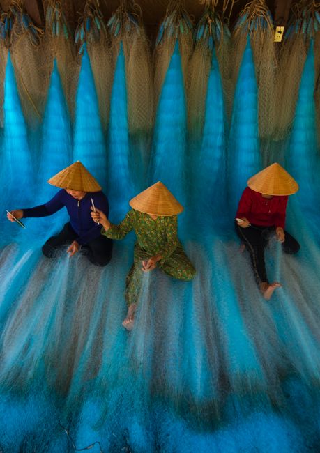Three workers create fishing nets, showcasing traditional craftsmanship in an overhead view.