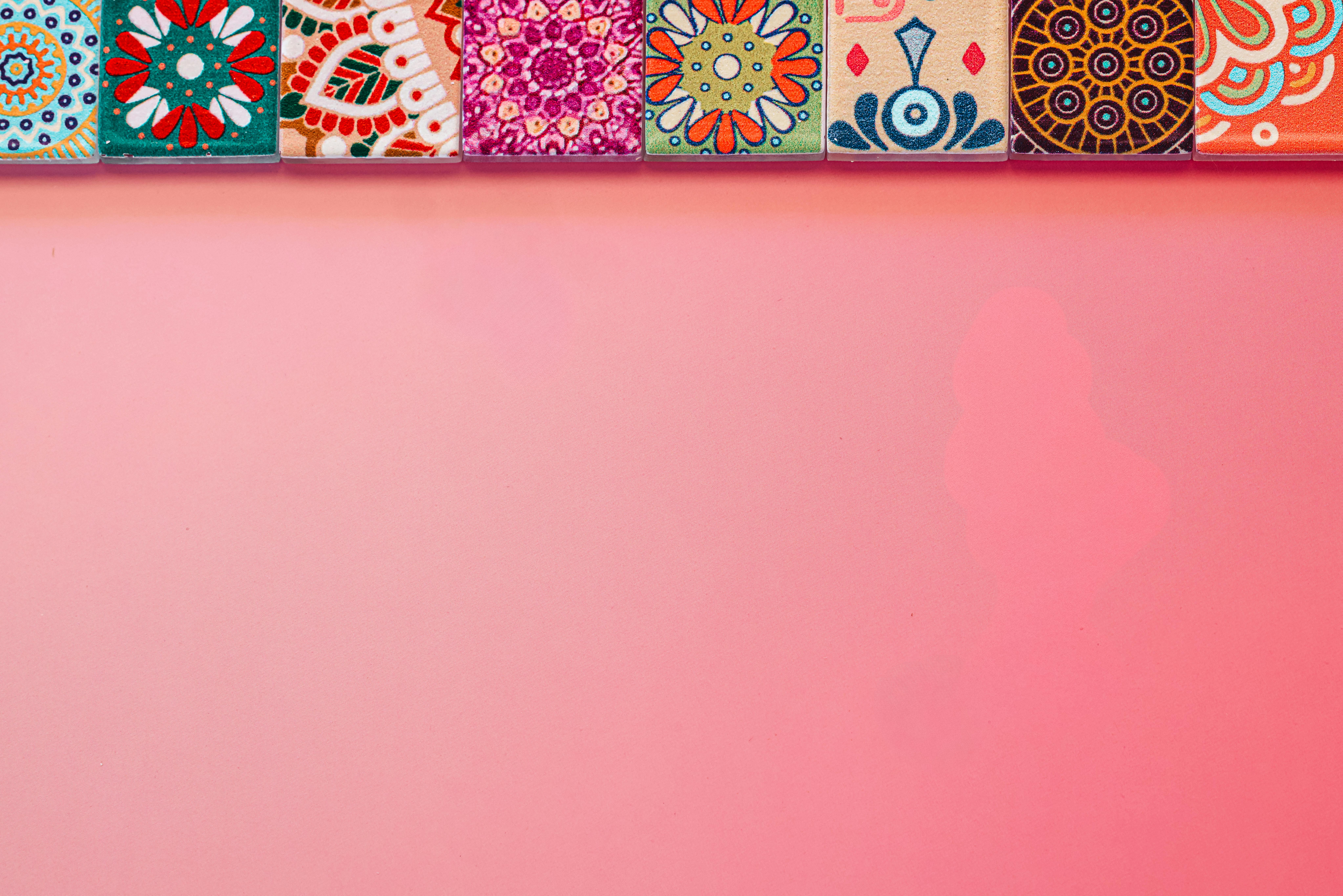 Gratis Azulejos de colores vibrantes con patrones intrincados sobre un fondo rosa pastel, perfectos para proyectos de diseño creativo. Foto de stock
