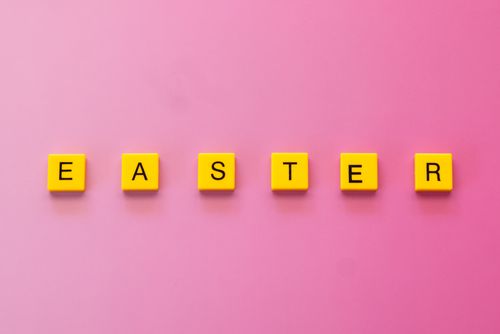 Free Bright yellow tiles spelling 'Easter' on a pink background, perfect for holiday themes. Stock Photo