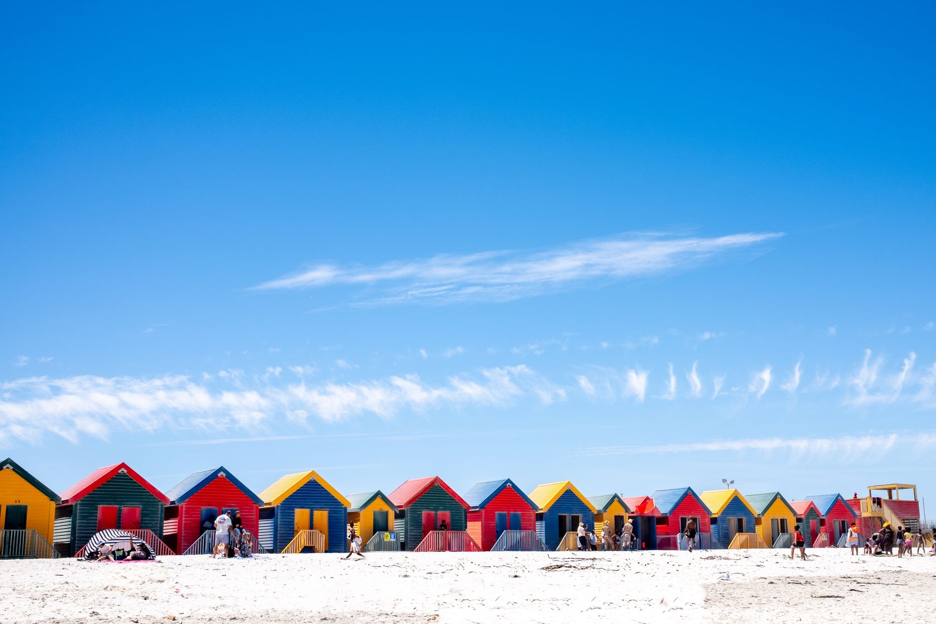 Vibrant beach huts at Muizenberg Beach under a clear blue sky, ideal for travel and architecture themes.