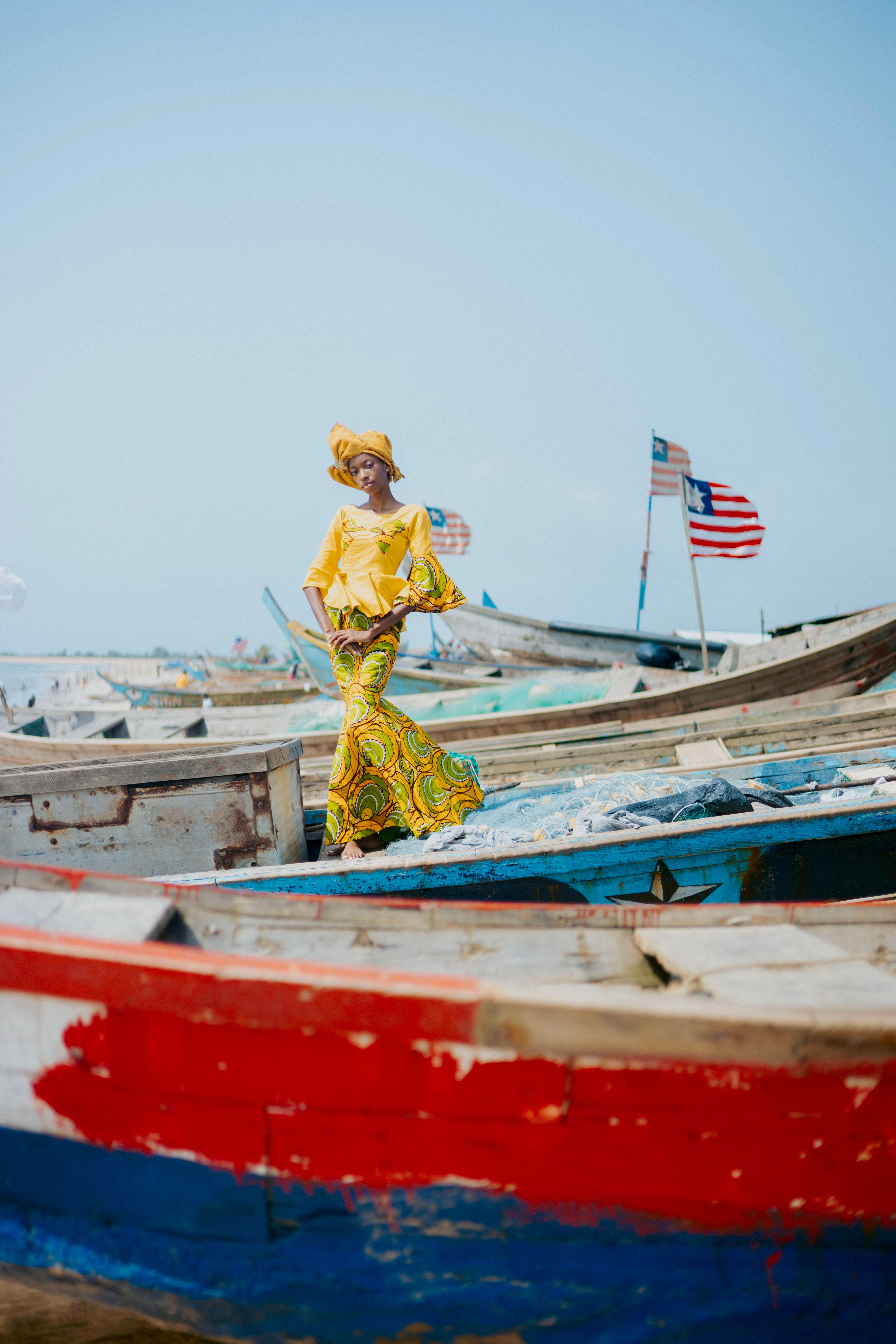 A woman in traditional attire stands on a fishing boat in Monrovia, Liberia, with flags in the background.